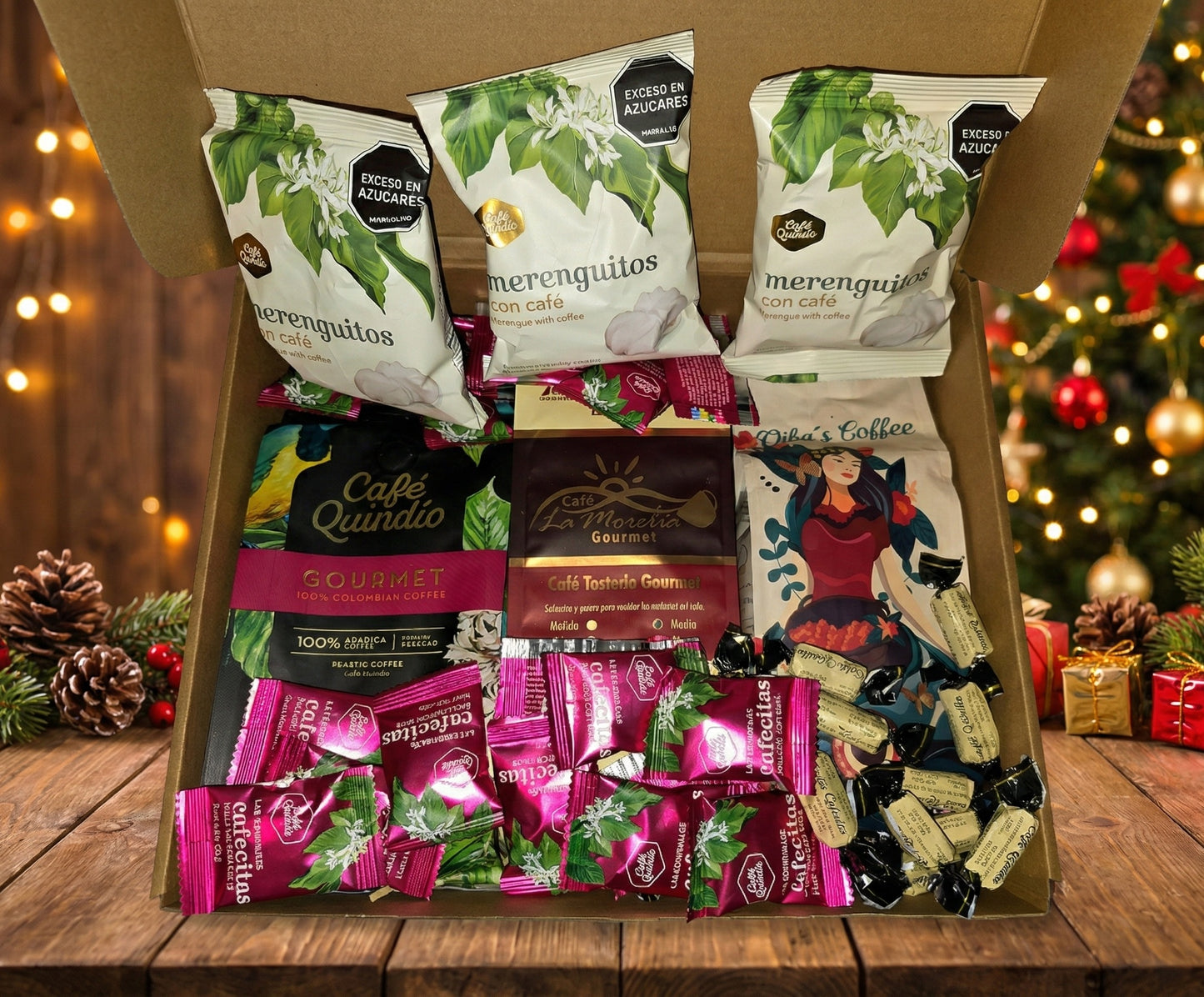 Open cardboard gift box displayed on a wooden table, filled with Colombian coffee products including three bags of Café Quindío coffee meringues, bags of Gourmet coffee from Café Quindío, La Morelia, and Oiba’s Coffee, and an assortment of coffee-flavored candies, set against a festive Christmas tree background. ground coffee