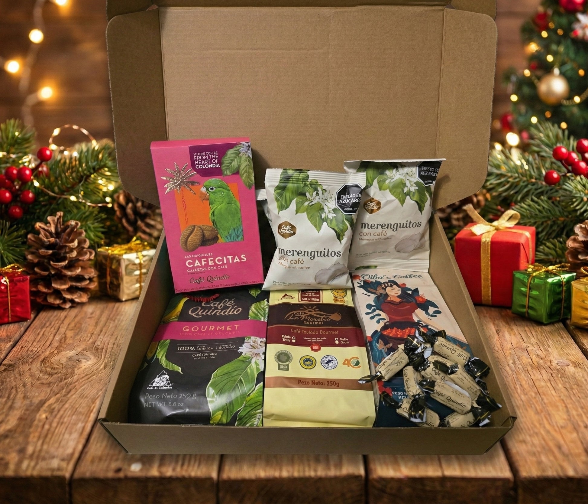 Open cardboard gift box displayed on a wooden table, filled with Colombian coffee products including three bags of Café Quindío coffee meringues, bags of Gourmet coffee from Café Quindío, La Morelia, and Oiba’s Coffee, and an assortment of coffee-flavored candies, set against a festive Christmas tree background.